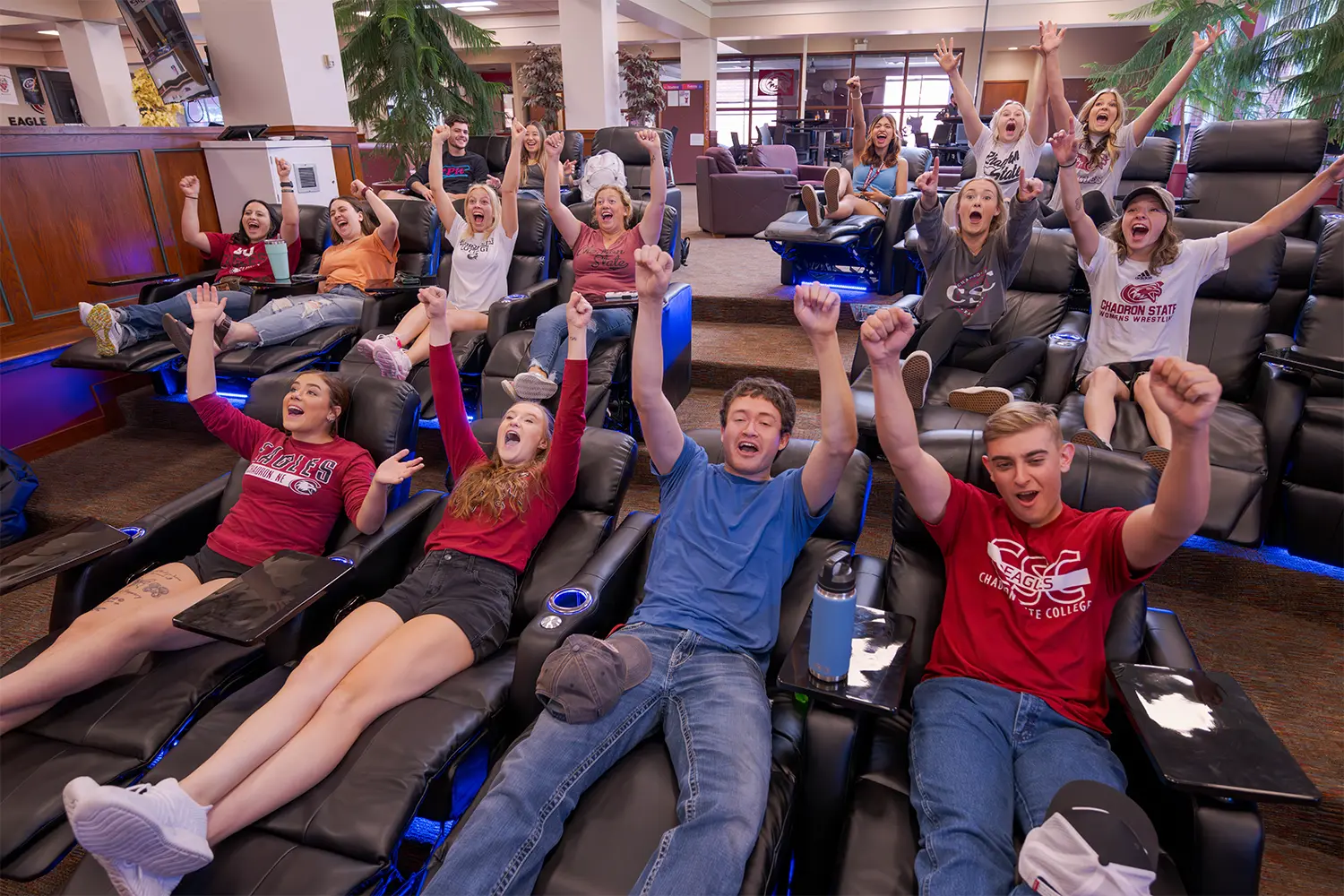 A large group of students cheer while watching TV