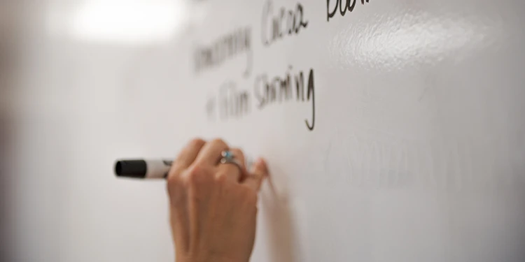 A close up of a hand writing on a white board