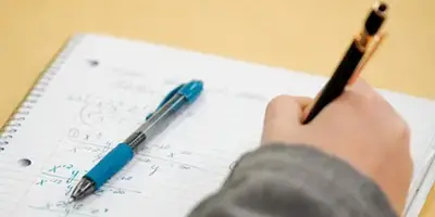 A close up of a hand writing math in a notebook