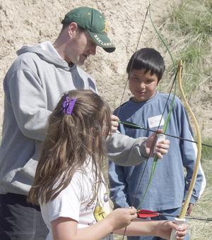 Chadron State senior Karl Norgard presents archery basics to fourth-graders Angel Davis and Joe Catches.