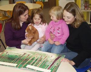 Siobhana McEwen (left), holding her sister Evelyn, and Laura Brooks, holding her cousin Madison Cogdill, look over a book about Teddy Bears in the Child Development Center at Chadron State College.