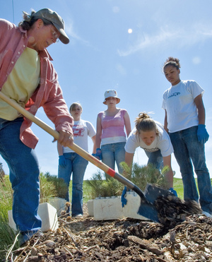 Lucinda Mays handles the shovel while the four Girl Scouts help set the seedlings in the arboretum at Chadron State.