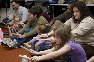 Children and their parents use rhythm sticks while singing at Musikgarten