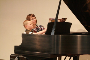 A student and young boy play the piano