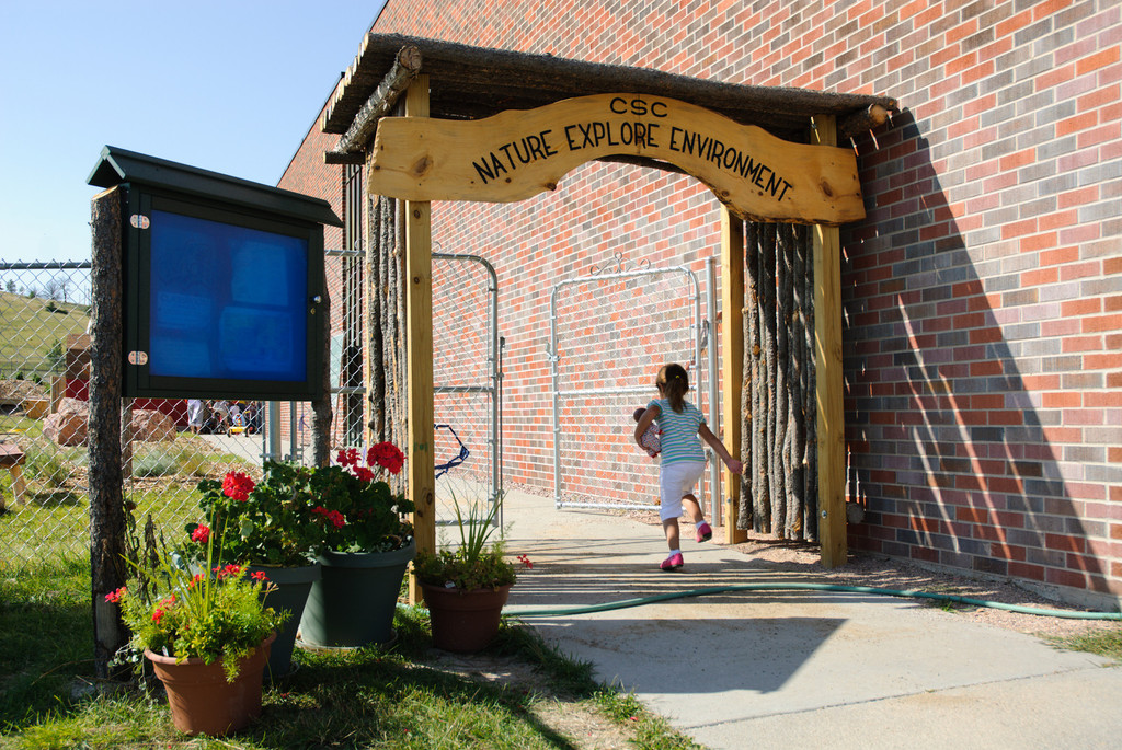 A child heads through the gate leading to the Nature Explore Learning Environment at the Child Development Center.