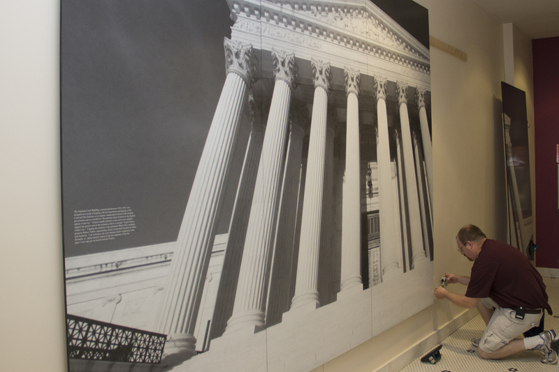 Nicholas Traub, graphic designer for Traub Design Associates, mounts an image of the Supreme Court Building, which is located near the Chadron State College Justice Studies Department's offices in Old Admin. (Photo by Justin Haag)