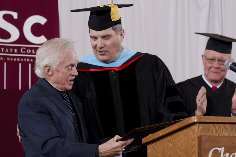 Randy Rhine, Chadron State College interim president, presents the Honorary Doctor of Humane Letters degree to Ron Hull of Lincoln, at left. Giving applause is Gary Bieganski, member of the Nebraska State College System Board of Trustees. (Photo by Tiffany Valandra)