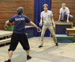 Three theatre students practice a sword fighting scene