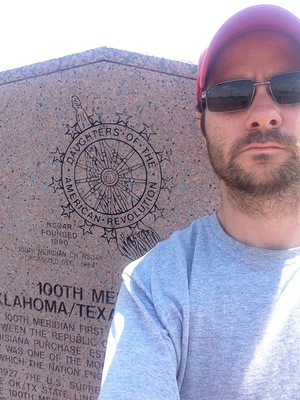 Dr. Steve Coughlin posing with 100th Meridian Marker