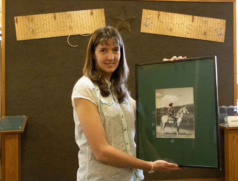 Chadron State College graduate Holly Counts poses with a circa 1940 photo of Mari Sandoz riding an Arabian horse owned by Lynn and Rose Van Vleet at their Nederland, Colorado, horse farm.