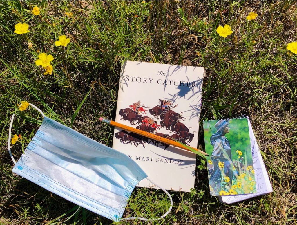 A mask, pencil, book and notebook lay in grass