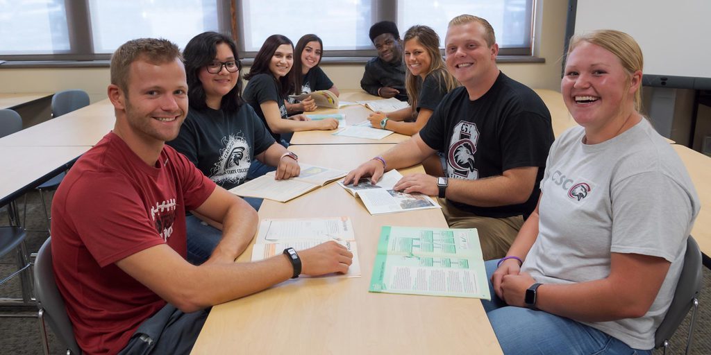 CSC students sitting at a desk studying and smiling for the camera