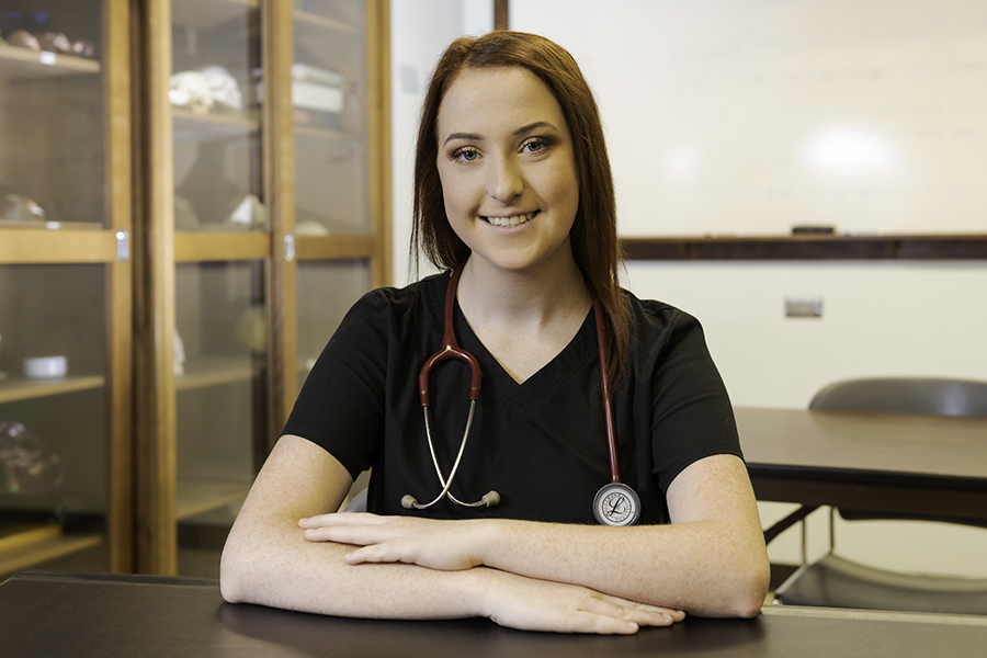 A young nursing student sits at a desk and smiles