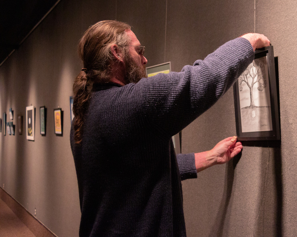 Matthew D. Reese, youth transition worker with Cirrus House, prepares the exhibit  in Memorial Hall's Main Gallery.