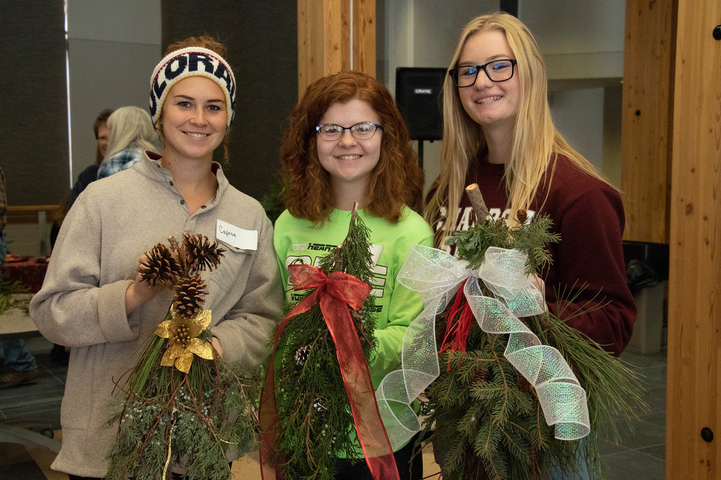 Three CSC students pose holding bouquets of pine tree limbs to make wreaths.