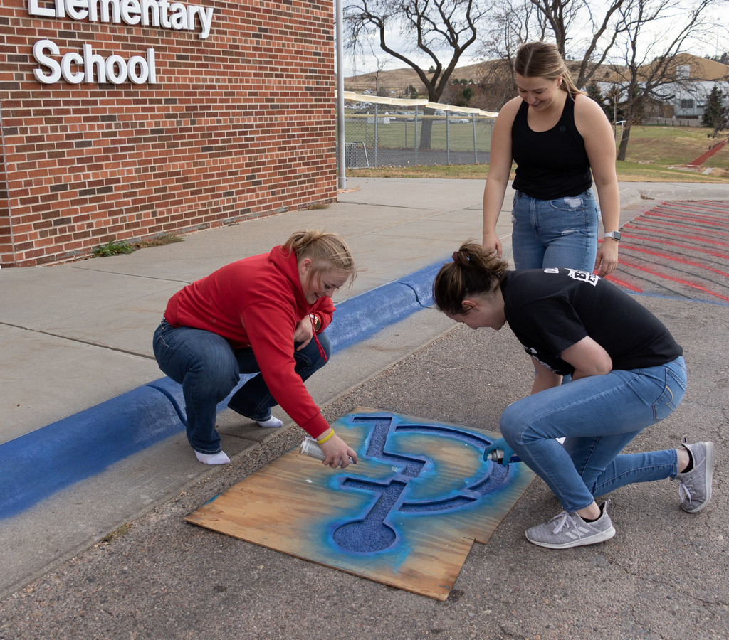 Three CSC students help to paint a handicapped parking space in front of Chadron Primary School.