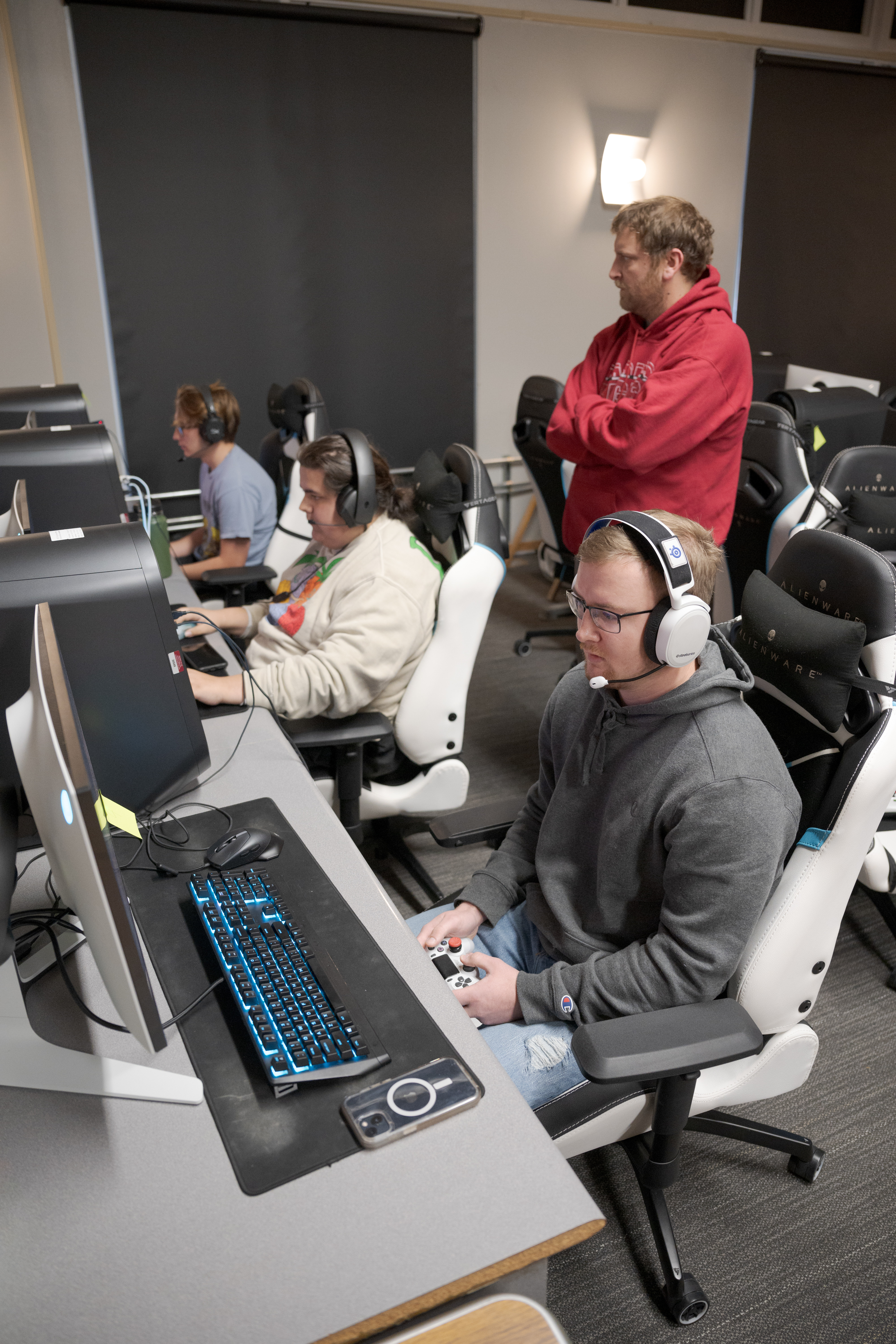 Three students sitting at computers, one adult standing