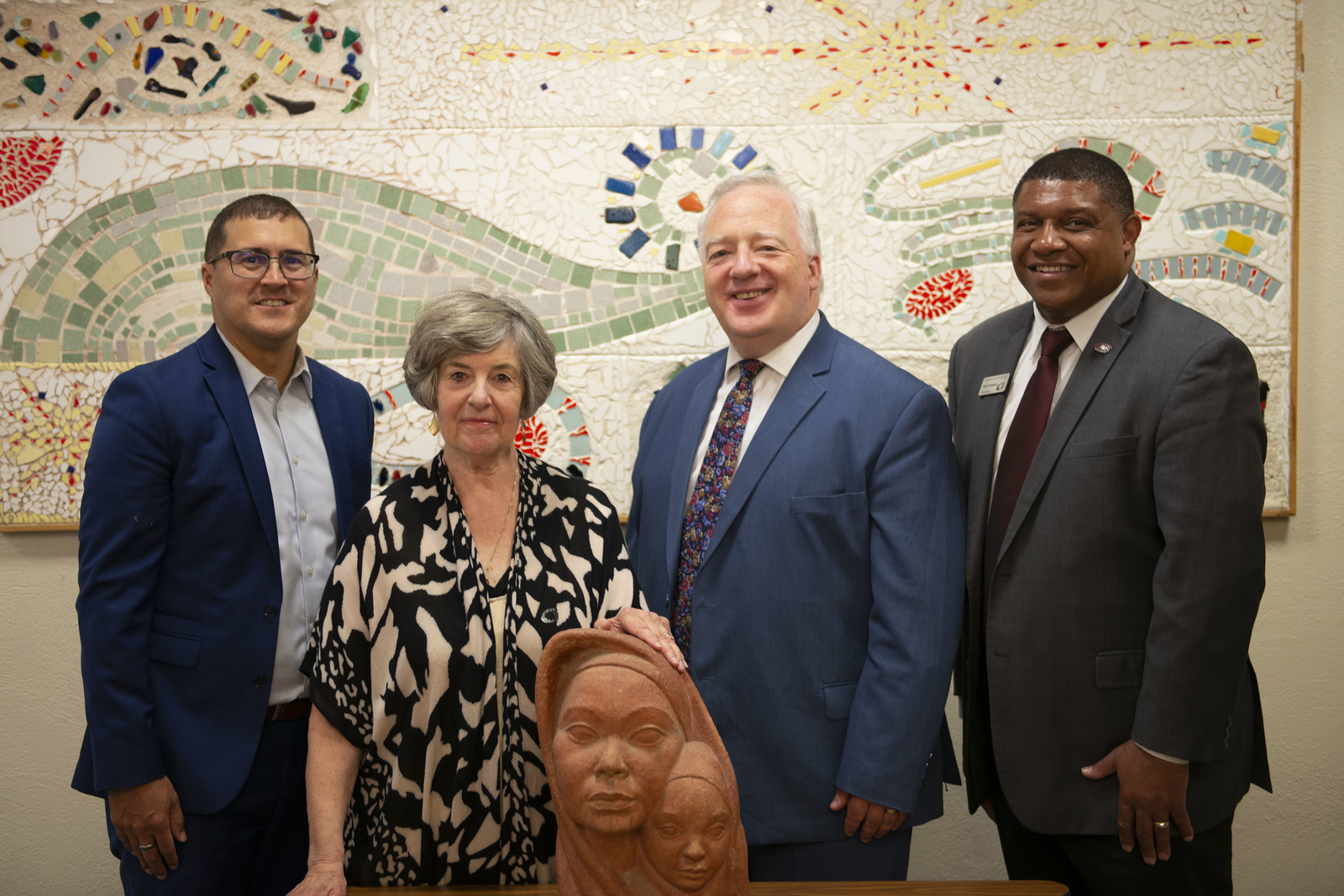 Four people posing with a clay sculpture