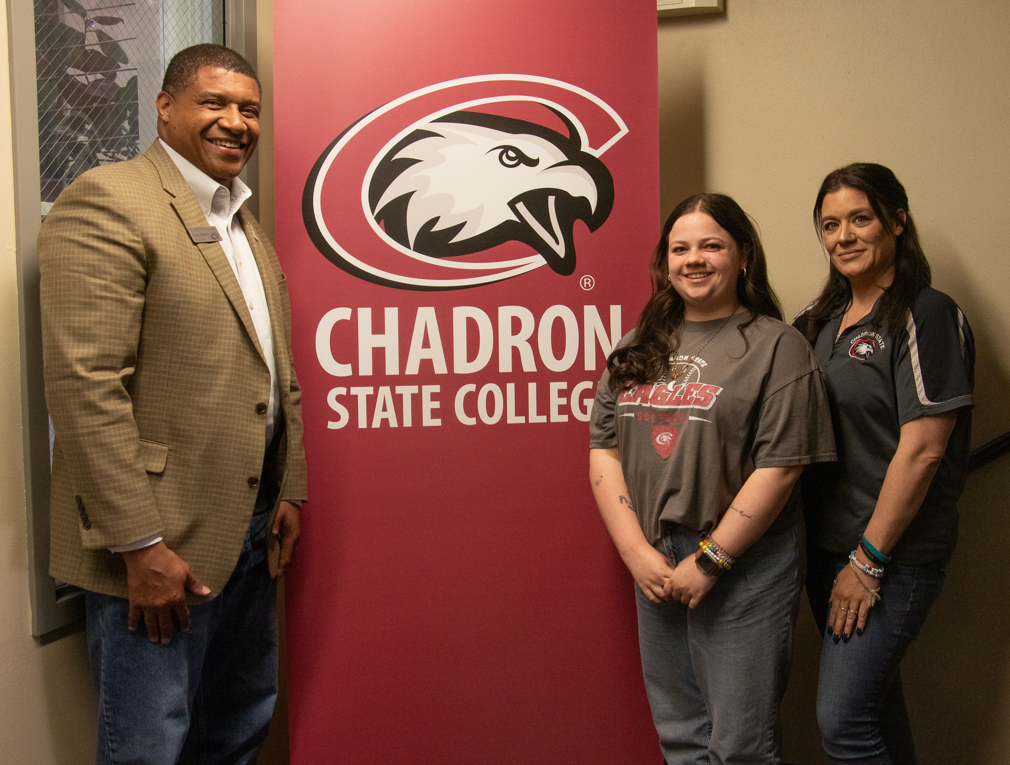 Three adults standing next to an indoor banner