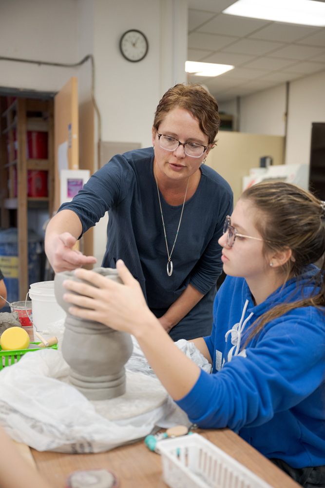 Woman teaching student how to work clay on a wheel