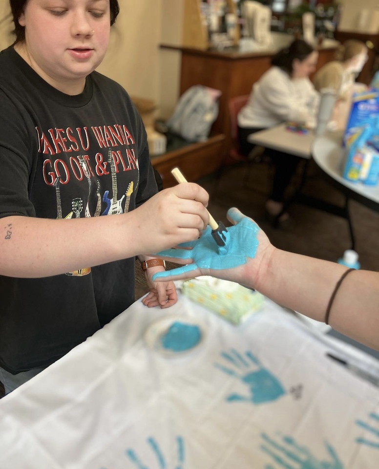 One woman painting anothr woman's hand teal