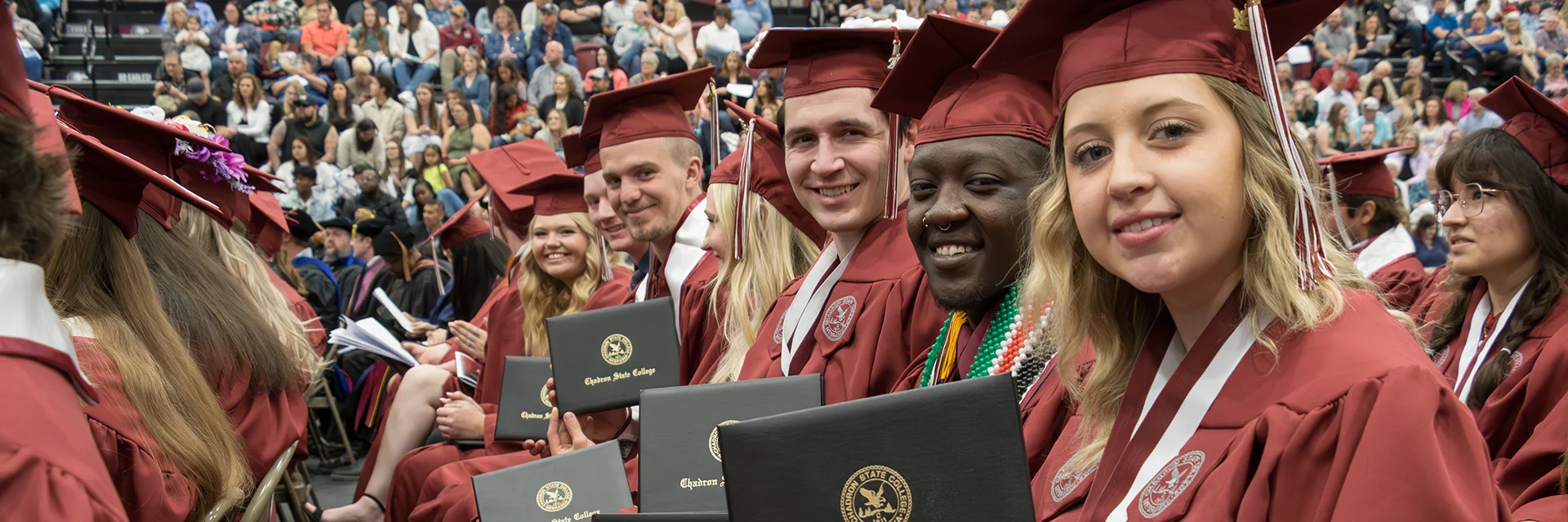 Group of college students at graduation smiling and showing their diplomas