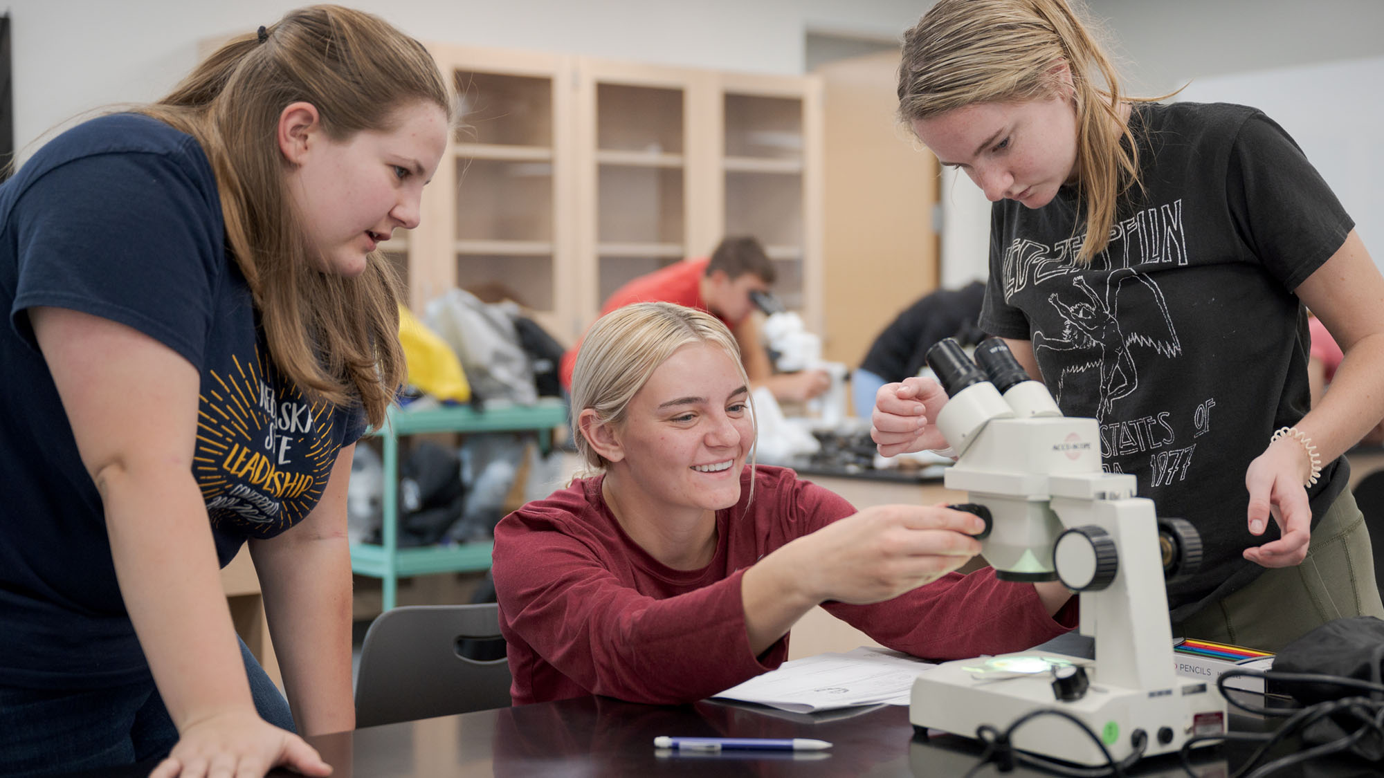 Three students work with a sample at a microscope