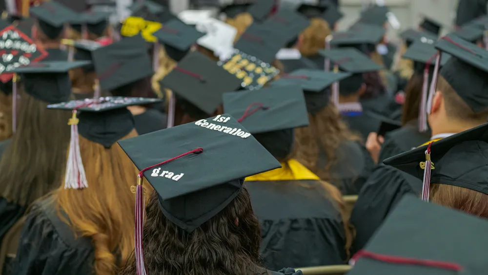 View overlooking many graduate mortarboards, one labeled First Generation Grad