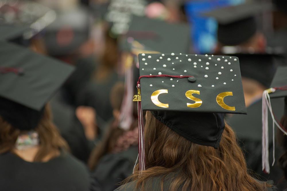 Student at graduation with a cap decorated to read CSC